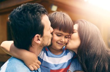 Mutlu aile, sevgi ve ebeveynler bakımı, kaynaşması ve birlikte rahatlaması için çocuğu dışarıda öperler. Gülümse, anne ve baba ve çocuk arka bahçede destek, bağ ve sağlıklı ilişki için sarılacaklar..