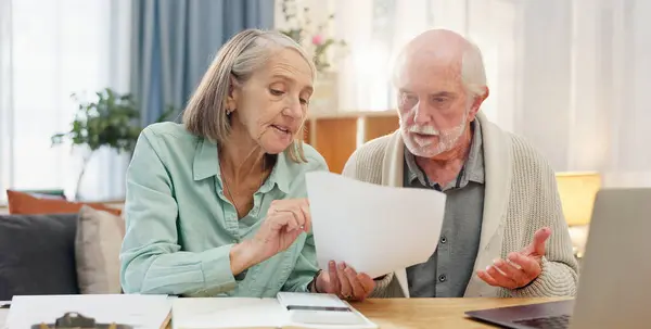 stock image Home, laptop and elderly couple with documents in discussion for financial bills, insurance and plan. Tech, retirement and senior people with paper by table for healthcare debt, invoice and budgeting.