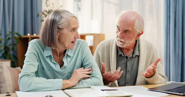 stock image Home, table and elderly couple with documents in discussion for financial plan, insurance and bills. Tech, retirement and senior people with paper by laptop for healthcare debt, invoice and budgeting.