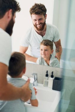 Banyo, baba ve çocuk ellerini destekle yıkıyor, gülümsüyor ve aynada sağlıklı hijyen öğretiyor. Temizlikçi, mutlu çocuk ve baba evde rutin, sağlık ve cilt bakımına hazırlanıyorlar.