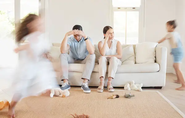 stock image Lounge, stress and parents with kids, running and frustrated of responsibility of children and chaos. Living room, playing and mess by girls, home and burnout of mother, father and tired of energy.