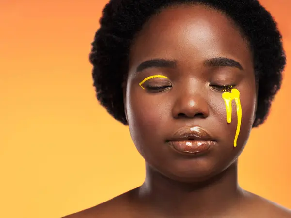 Stock image Black woman, tears and makeup or paint on studio background with cosmetics, resilience and strong. African girl, crying and gold eyeliner with glow, shine and pain on backdrop for empowerment.