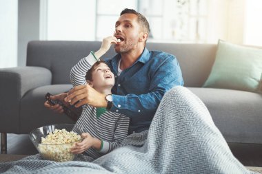 Baba, televizyon kumandası ve kanepede patlamış mısırlı çocuk eğlence, atıştırma ve çizgi film izlemek için birlikte. Aile, baba ve oğul evde bakım, sevgi ve gösteri için oturma odasında besleniyorlar..