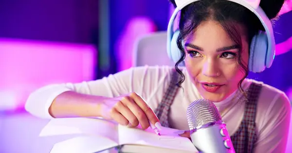 stock image Influencer, ASMR and book with microphone, whisper and neon lights with podcast, content creation and tech. Home, broadcast and pen writing for stress relief with woman and recording for sound.