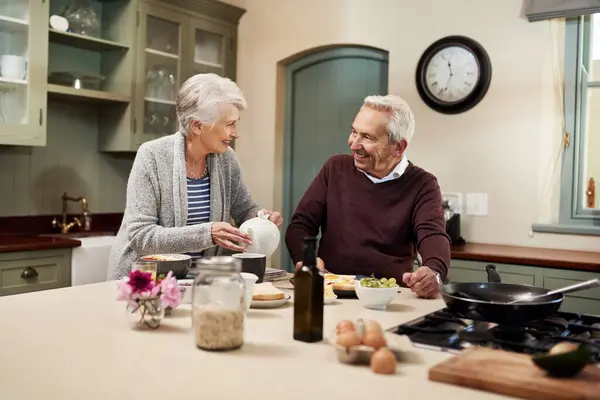 stock image Senior couple, kitchen and eating together on countertop, bonding and breakfast for food and coffee. Home, happy or married people in house for brunch in retirement, ingredients and support with love.