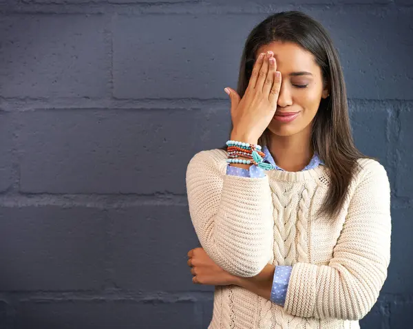 stock image Woman, smile and hand on face with forget information, thinking and stupid emoji by brick wall mockup. Female person, happy and remember with embarrassing memory, space and oops by dark background.