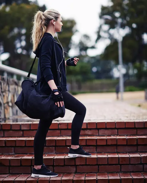 stock image Gym, bag and woman with headphones outdoors for workout, music and travel to sports practice. Morning, fitness and athlete with thinking by staircase for exercise, training and wellness podcast.