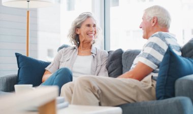 Mature couple, home and smile on sofa in living room on break, bonding and relax. People, relationship and laughing for happy with gossip for conversation, chat and funny memories on couch with care.