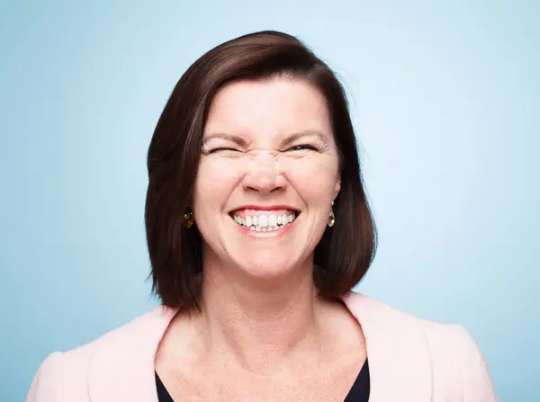 stock image Comic model, portrait and happy with crazy face, positive and fun for comedic relief. Mature woman, blue background and joyful for healthy teeth, upbeat and excited with goofy look for laughter.