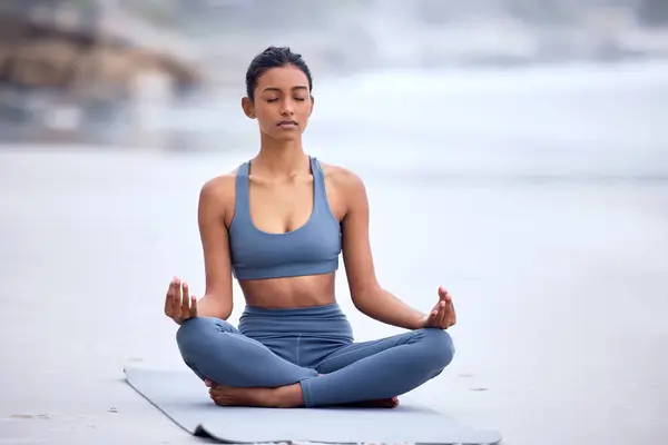 stock image Calm woman, yoga and beach mediation with lotus pose for wellness, zen mindset and spiritual balance. Female athlete, fitness and peace to meditate, relax and breathe for mental health in nature.