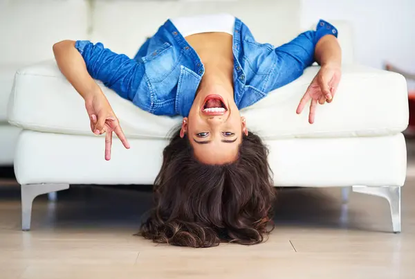 stock image Peace sign, portrait and woman upside down on sofa in living room of home for weekend break. Emoji, hand gesture or smile and happy person relaxing in apartment with energy or excited for time off.