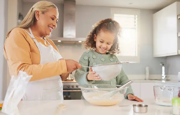 Happy, granny or girl child baking with help, lesson or food for learning ingredients in family home. Sifter, dessert or grandmother teaching kid cooking skills for development or breakfast recipe.