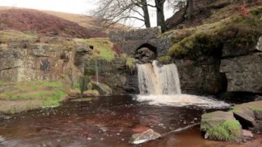İngiltere, İngiltere 'de Peak District Ulusal Parkı' ndaki Three Shires Head 'de şelalenin ve yük atı taş köprüsünün kırsal bir manzarası..