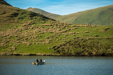 Anglers fishing from a boat on Llyn Dywarchen in the Eryri National Park, Wales with Yr Wyddfa in the distance. clipart