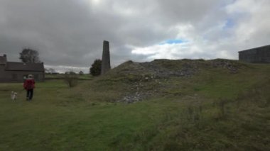 SHELDON, DERBYSHIRE, İngiltere - 17 Ekim 2024: Magpie Madeni 'nde köpeklerini gezdiren kırmızı ceketli bir kadın, İngiltere, İngiltere' deki Peak District Ulusal Parkı 'nda.