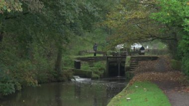 STOKE-ON-TRENT, STAFFORDSHIRE, ENGLAND - 30 EKİM 2024: Erkek ve kadın Caldon kanalında kilit açarken bir çocuk dar kayığı kullanıyor.