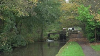 STOKE-ON-TRENT, STAFFORDSHIRE, ENGLAND - 30 EKİM 2024: Erkek ve kadın Caldon kanalında kilit açarken bir çocuk dar kayığı kullanıyor.