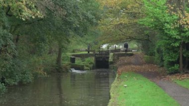 STOKE-ON-TRENT, STAFFORDSHIRE, ENGLAND - 30 EKİM 2024: Erkek ve kadın Caldon kanalında kilit açarken bir çocuk dar kayığı kullanıyor.