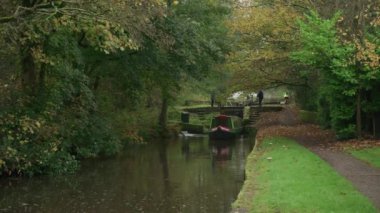 STOKE-ON-TRENT, STAFFORDSHIRE, ENGLAND - 30 EKİM 2024: Erkek ve kadın Caldon kanalında kilit açarken bir çocuk dar kayığı kullanıyor.