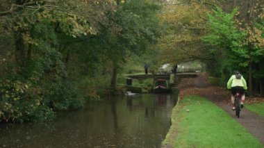 STOKE-ON-TRENT, STAFFORDSHIRE, ENGLAND - 30 EKİM 2024: Erkek ve kadın Caldon kanalında kilit açarken bir çocuk dar kayığı kullanıyor.
