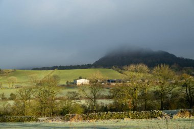 A bleak atmospheric rural winter landscape of Hen Cloud shrouded in low cloud in the Peak District, England, UK. clipart