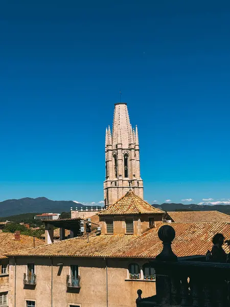 Arka planda mavi gökyüzü ve çan kulesi olan yüksek bir bina. Bina kahverengi ve bir sürü penceresi var.