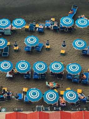 Bir sürü mavi ve beyaz şemsiyeli ve sandalyeli bir plaj sahnesi. Sahne rahat ve sakin.