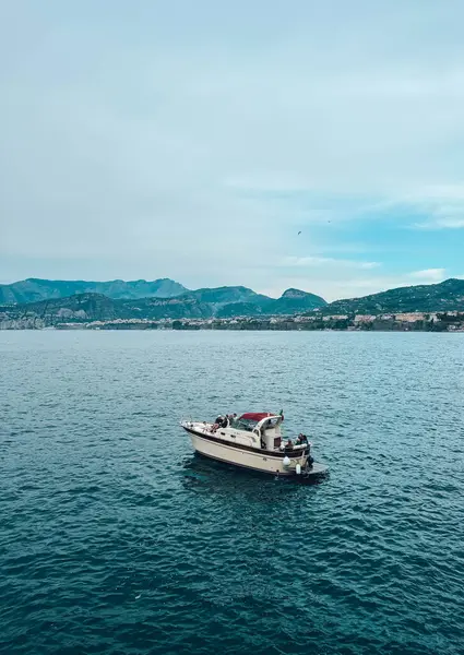 Bir dağ sırasının önünde suda yüzen bir tekne var. Gökyüzü açık ve su sakin.