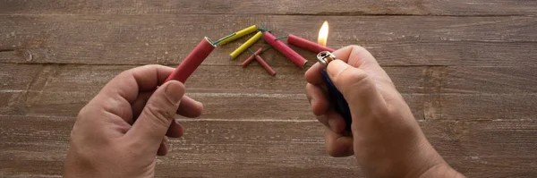 Image of the hands of a man who lights the fuse of a firecracker with a lighter. Reference you have celebrations and the danger of the barrels. Horizontal banner