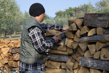 Soğuk ve kış beklentisiyle odun stoklayan bir adam. Evi yakacak odunla ısıtmaya gönderme yap. Ev ısıtmasının maliyetinden tasarruf.