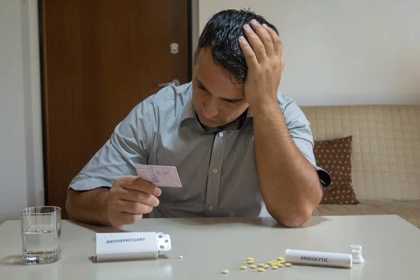 Worried man with hand in hair holding driving license with medicines like antidepressants and anxiolytics on the table. Effect of certain medicines on health and driving reflexes
