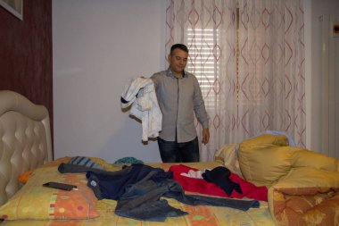 Yatak odasında kıyafetlerini yatağa atan bir adamın görüntüsü. Dağınık yatak odası ve dağınık adam.