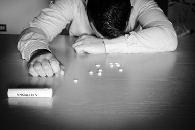 Kafası masanın üzerinde dinlenen bir adam görüntüsü ve etrafa yayılmış bir tüp anksiyete ilacı ve ilaç. Psikotropik uyuşturucu kullanan adam.