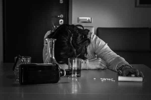 Image of a young woman passed out on the table after abusing alcohol and psychotropic drugs. Reference to the abuse and dependence of these substances.