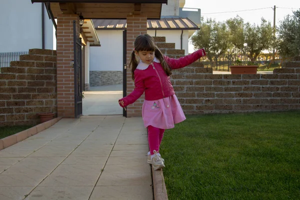 Image of an adorable little girl coming back from school playing walking on a curb while balancing.