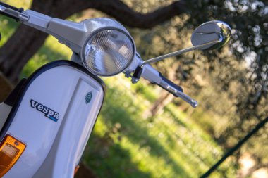 Close-up image of an old white colored Piaggio Vespa motorcycle.