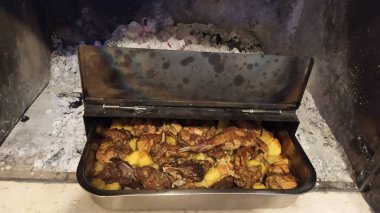 Image of a pan with meat and potatoes over hot coals in a fireplace. Typical Italian recipe in Abruzzo
