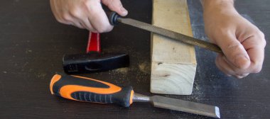 Image of the hands of a carpenter craftsman who smoothes a piece of wood with a rasp. Wood filing and cleaning. Horizontal banner 