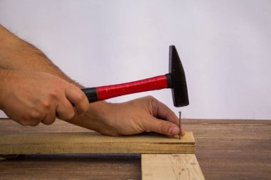 Image of a handyman craftsman's hands holding a hammer and nails while fixing wooden planks.