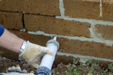 Image of the hands of a mason while filling joints in a tuff brick wall. Finishing work of DIY and construction. clipart