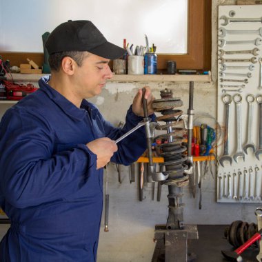 Bir araba amortisörünü ingiliz anahtarı ve sökücüyle sökerken atölyesinde çalışan bir tamircinin resmi.
