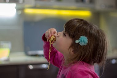 Elleriyle spagetti yiyen sevimli esmer bir kızın görüntüsü..