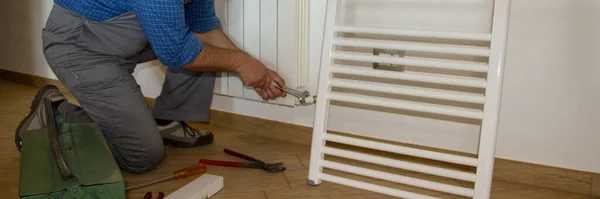 Image of a plumber in a house who mounts radiators with a wrench. Installation of heating for a house. Horizontal banner