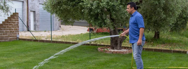 想象一个男人用软管浇灌他的花园 草坪的养护和维护 并提及水浪费和干旱问题 横向横幅 — 图库照片