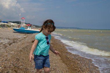 Deniz kenarında oynayan ve suya taş atan sevimli esmer bir kızın görüntüsü. İtalya 'ya sahil gezisi
