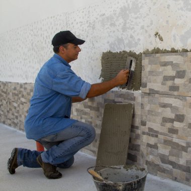 Elinde spatulası olan ve fayansları duvara yapıştırmak için yapıştırıcı döşeyen becerikli bir adam görüntüsü. Kendin-yap işi ve ev yenilemesi.