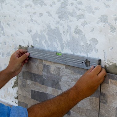 Yeni monte edilen fayansların doğruluğunu bir seviye ile kontrol ederken bir klasörün ellerinin görüntüsü. DIY işleri