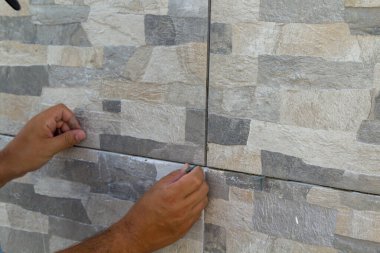 Yeni döşenmiş kiremitleri delen bir ustabaşının elleri. Kendin-yap işi, tadilat ve ev zemininin kurulumu. Yatay Pankart 