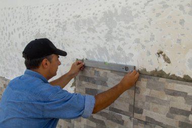 Fayansların doğru yerleştirildiğinden emin olmak için ruh seviyesini kullanan bir klasörün resmi. Kendin-yap restorasyon işi.