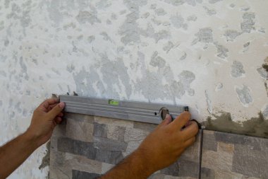 Yeni monte edilen fayansların doğruluğunu bir seviye ile kontrol ederken bir klasörün ellerinin görüntüsü. DIY işleri